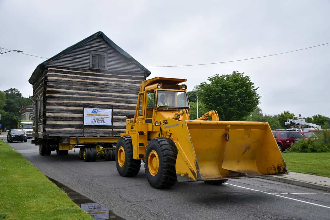 Corin Chapman__DSC0092 Old wooden house being transported on a flatbed trailer, with a yellow front loader assisting.