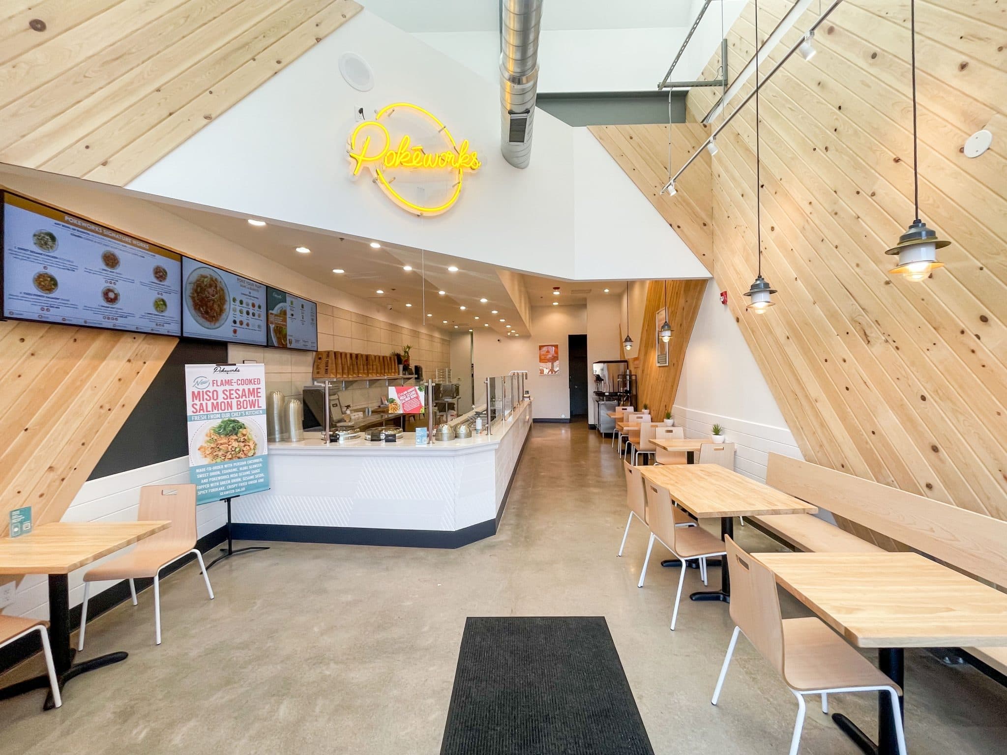 Pokeworks restaurant interior with wood-paneled walls, menu screens, and dining tables in Denver. Showcasing real estate layout