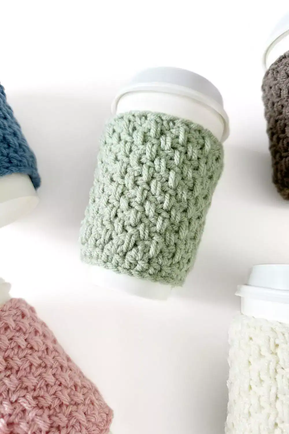 a group of crochet coffee cozies in soft pastel colours