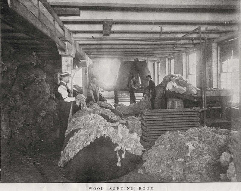 stephenson4 Wool sorting room in historic textile factory, workers handling raw wool, vintage black and white photograph, industrial revolution history, textile industry.