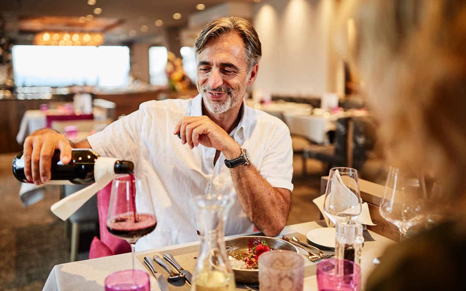 Mann schenkt einen Rotwein für seine Partnerin am Tisch ein