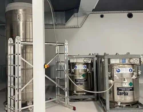 Large liquid nitrogen containers, crucial for cryopreservation, stand in a sterile lab setting. The tanks, labeled "Garba," store bodies for future revival, a core component of cryonics services. Ladders provide access for maintenance. The -196 degrees celsius storage is vital for body freezing.