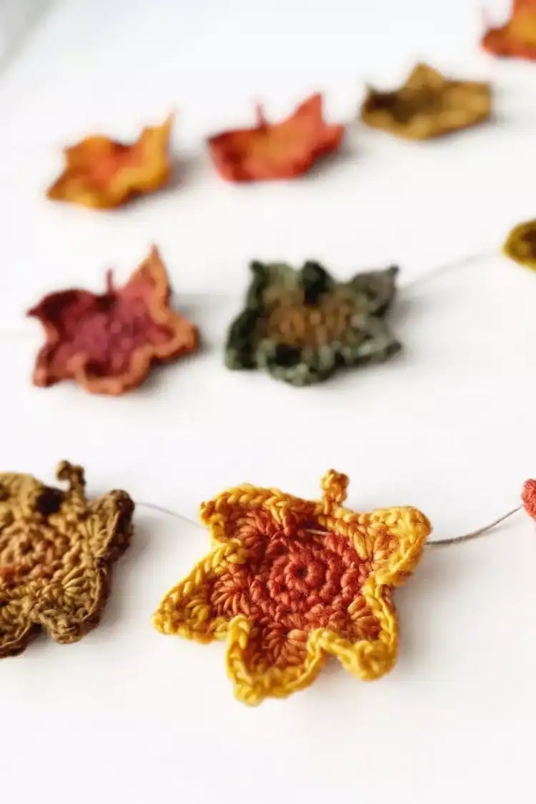 Close-up of a garland with crocheted autumn leaves in yellow, orange, red, brown, and green on a white background. Free crochet pattern