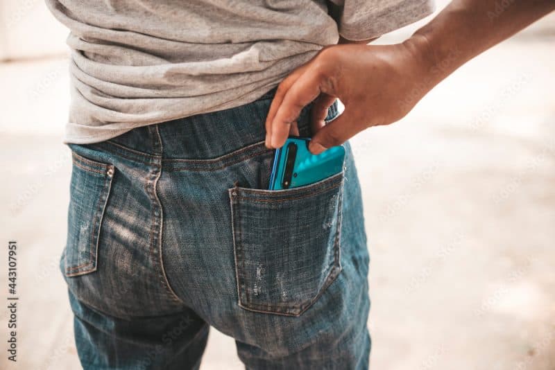 An anonymous thief attempts to covertly snatch a cellphone from a oblivious girl's back pocket.