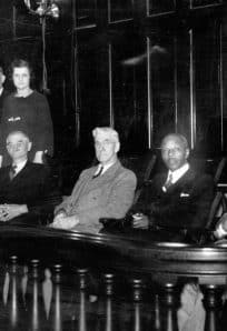 Grand Jury 1935 ph 318-1 compressed Historic photograph of distinguished guests and officials seated in a courtroom or council chamber, showcasing mid-20th century formal attire.