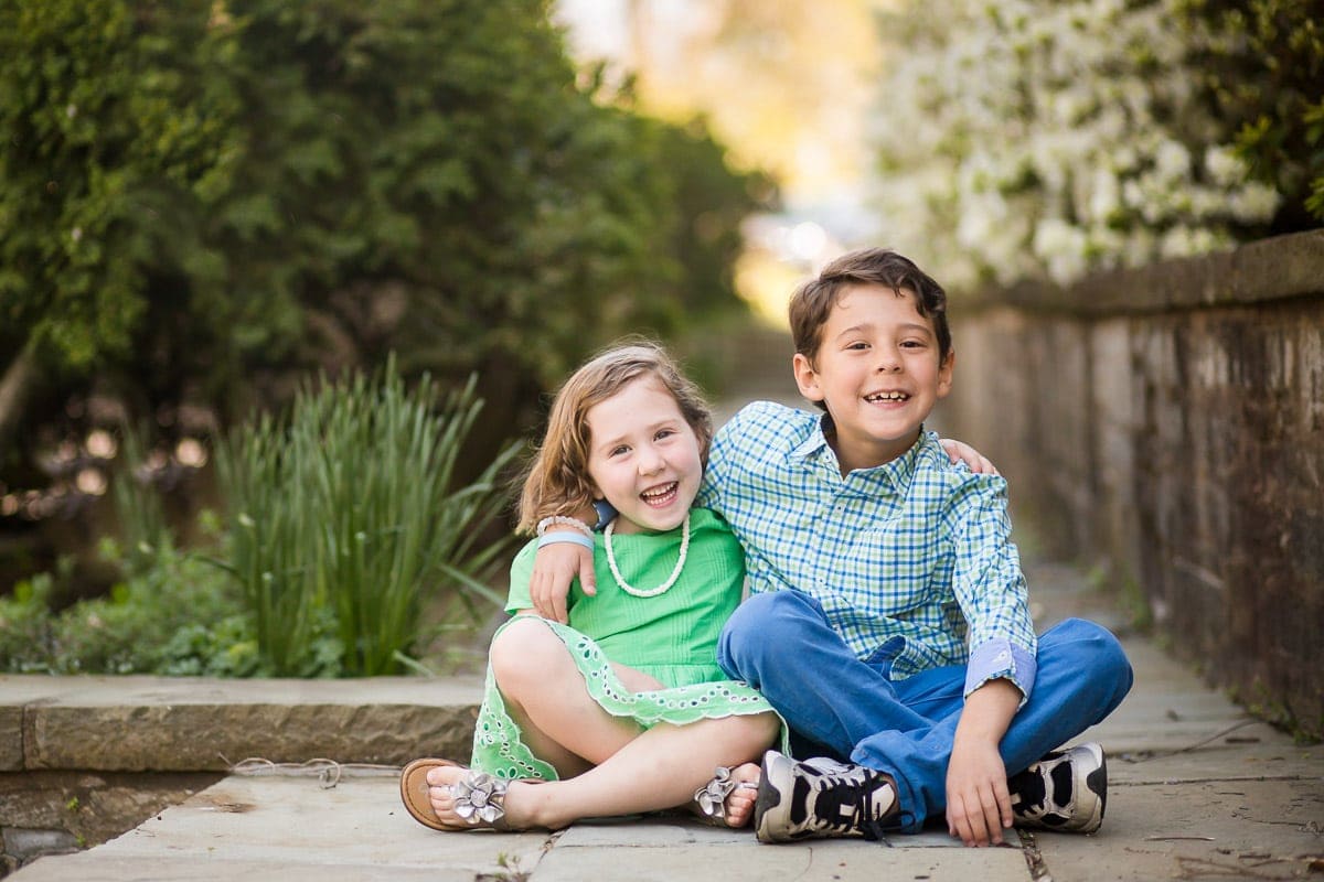 portrait of siblings sitting together on a stone walkway on the grounds of Washington National Cathedral