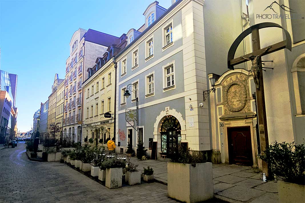 Ein christliches Kreuz steht am Rand einer Straße mit pastellfarbenen Fassaden