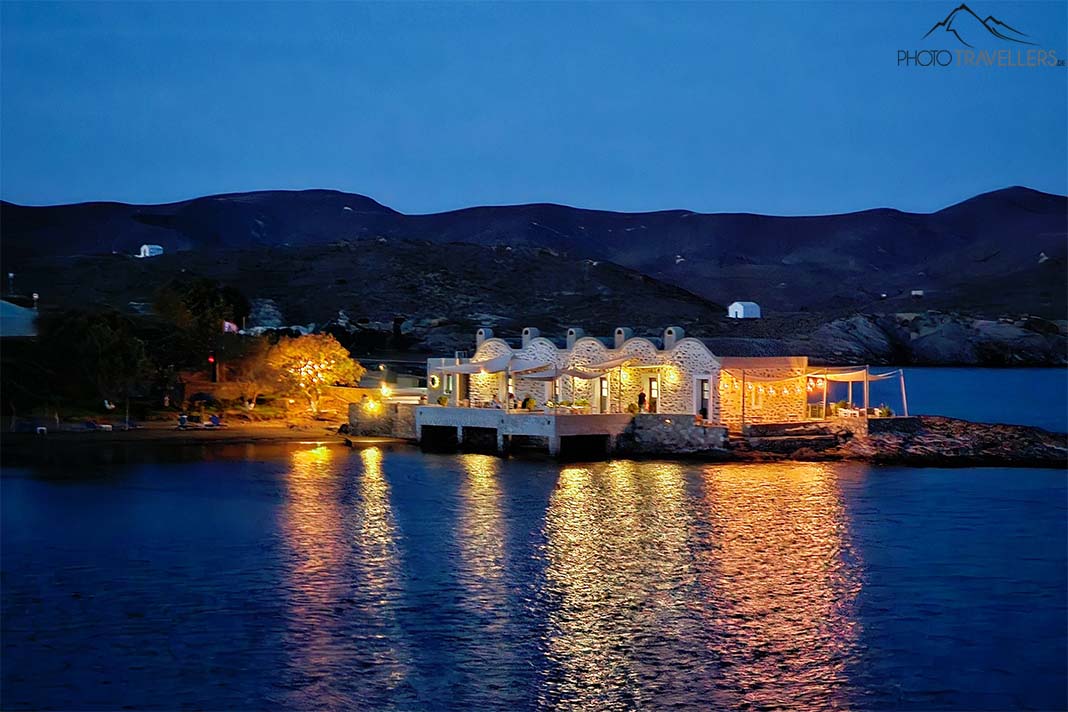 Mehrreihiges beleuchtetes Steinhaus mit Bögen im Nachtlicht auf einer vorgelagerten Insel