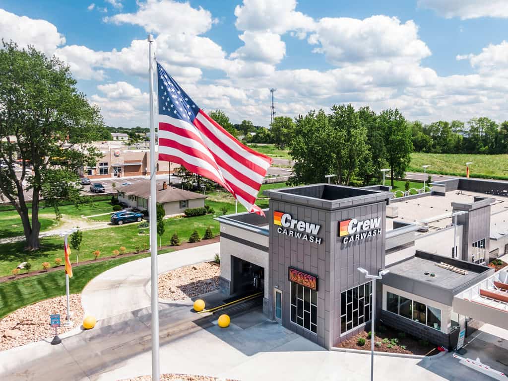 Crew Carwash location with American flag, featuring the company's logo and "Open" sign at the entrance.