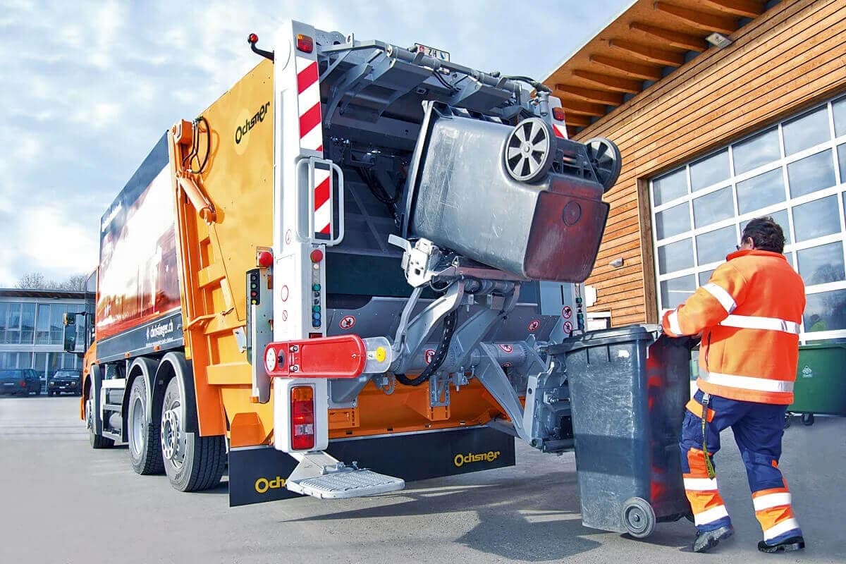 Arbeiter hängt eine Tonne an einem Müllfahrzeug ein