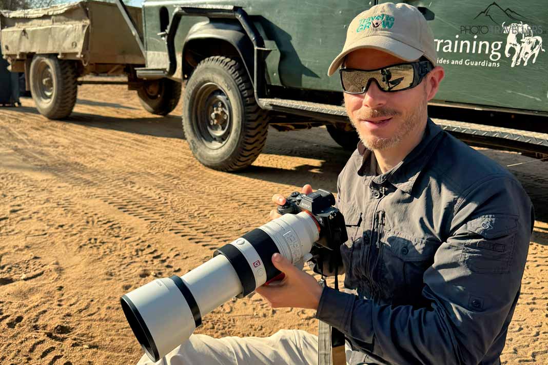 Profifotograf Florian Westermann mit einem Teleobjektiv vor einem Jeep in Südafrika