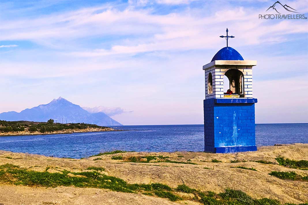 Ein blauer Gedenkstein mit Kuppel und Kreuz mit dem Berg Athos im Hintergrund