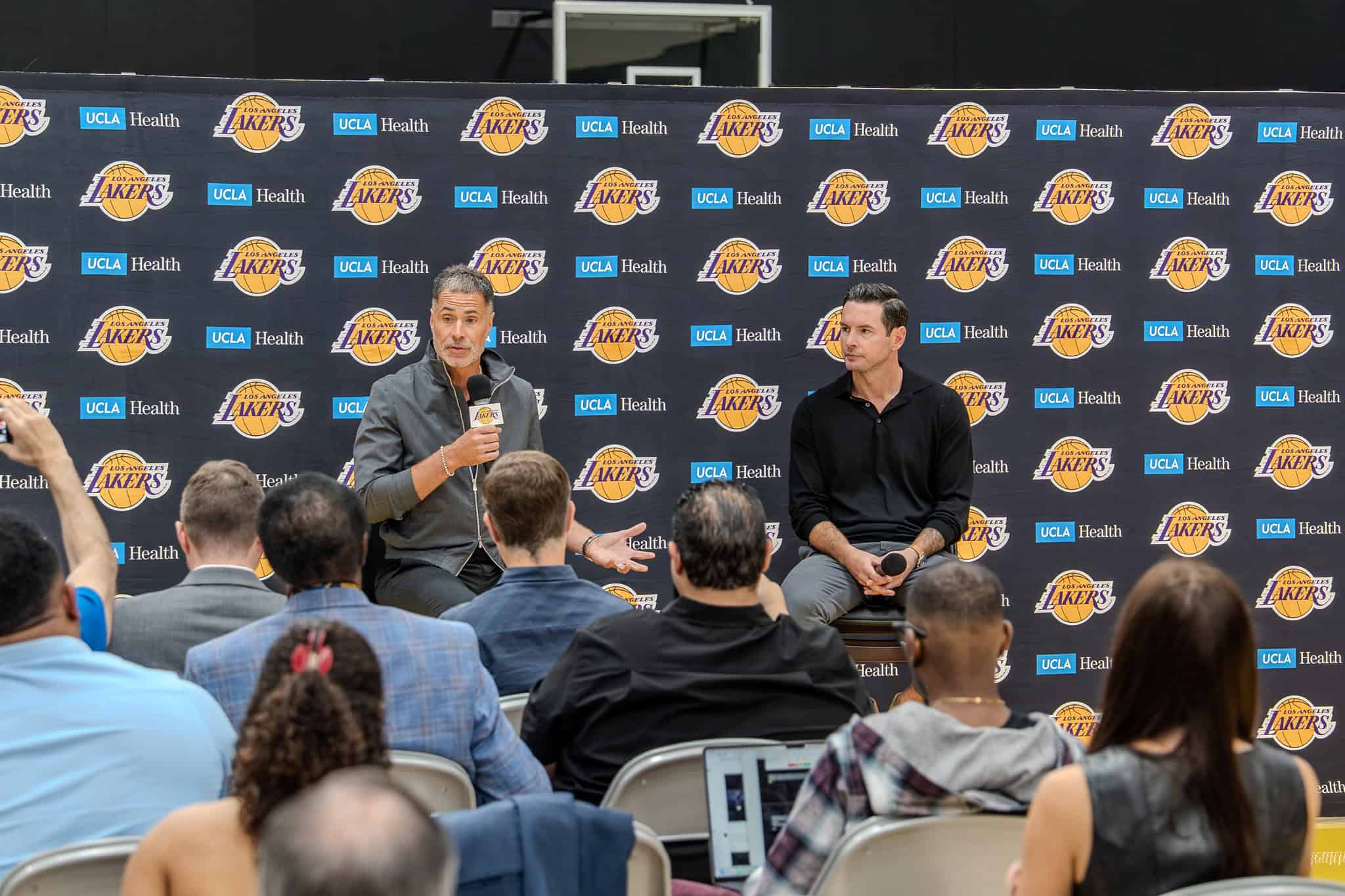 Rob Pelinka speaks during the Lakers 2025 press conference as JJ Redick listens, with media members seated in front