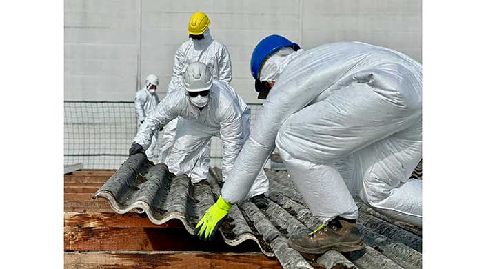 Arbeiter in Schutzanzügen und Helmen entfernen asbesthaltige Dachplatten.