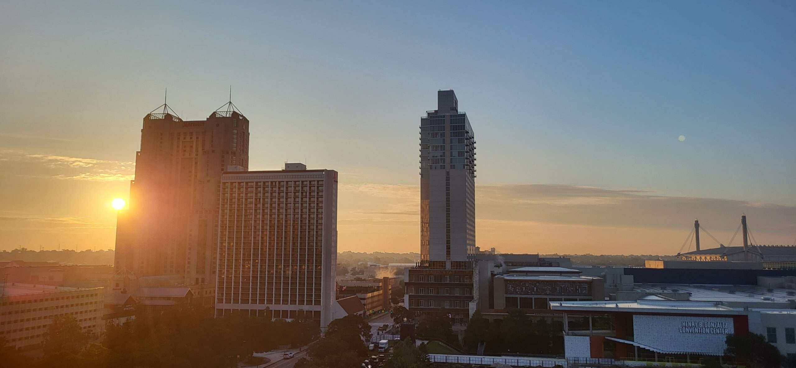 Sonnenuntergang über einer Skyline einer amerikanischen Stadt mit modernen Hochhäusern und einem Fluss im Vordergrund.