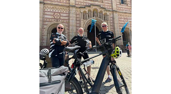 Zwei Radfahrer in schwarzer Kleidung stehen mit ihren Fahrrädern vor einem historischen Gebäude mit Bogen und Verzierungen.