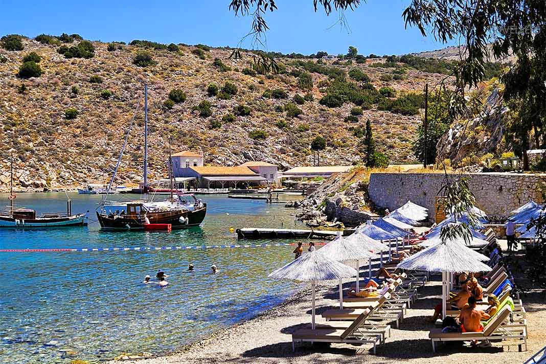 Sonnenliegen und Schirme reihen sich vor Booten am Mandraki-Beach aneinander