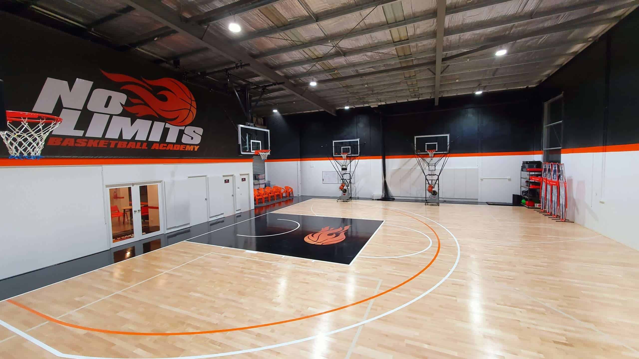 Bright indoor basketball court with "No Limits Basketball Academy" branding and modern training equipment.