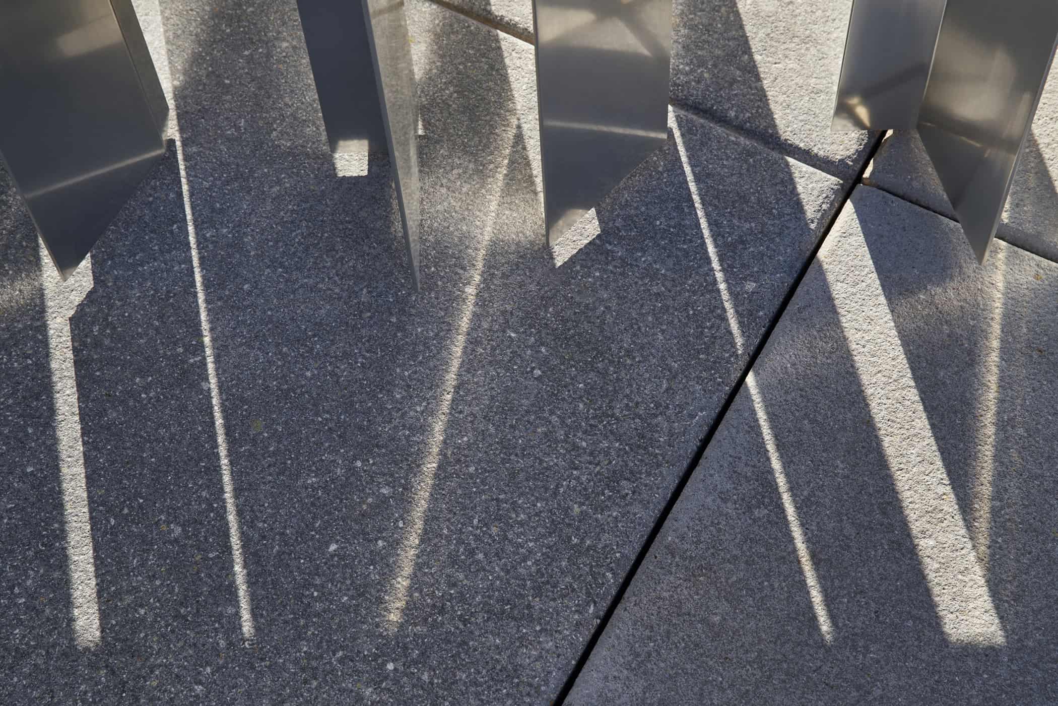 Close-up of vertical aluminum fins casting sharp, angular shadows on the concrete pavement at the Oklahoma Contemporary Arts Center.