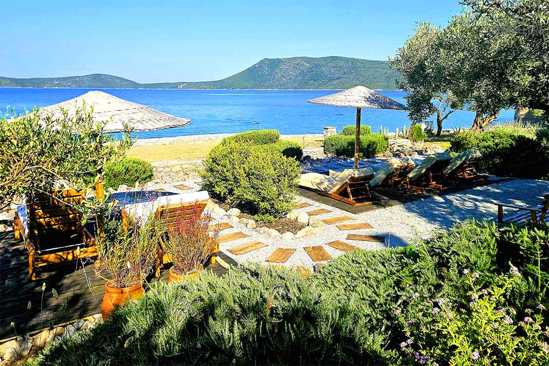 Wenige Holzliegen und Sonnenschirme an einem begrünten Garten am Glifa Strand in Alonnisos