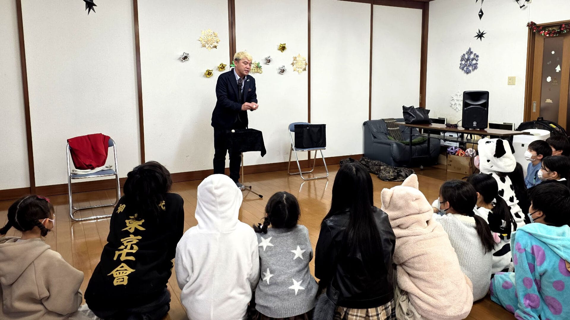 氷見市の学童でクリスマスショー!「人は鏡」を実感 1 氷見市の学童保育で開催されたクリスマス会で、マジックを披露して子供たちを驚かせるマジシャン・コンプレッサーの様子