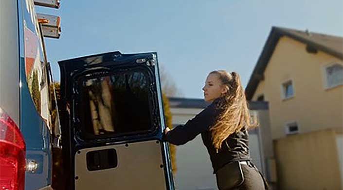 Eine Person öffnet die Heckklappe eines Lieferwagens bei Tageslicht im Freien.