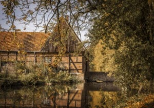 Hochzeitslocation Haus Runde 5 Backsteinhaus mit Ziegeldach an einem Teich, perfekte Eventlocation inmitten herbstlicher Bäume.