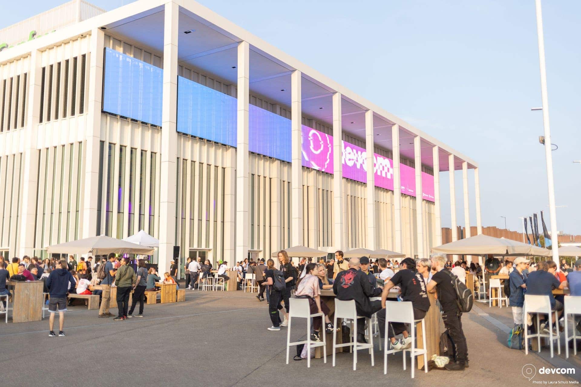 devcom2024_102 Rencontre gaming en extérieur devant un bâtiment moderne avec écrans lumineux, ambiance digitale et communauté passionnée, événement e-sport, gaming live, lieu de rassemblement gaming, accès Wi-Fi haute vitesse.