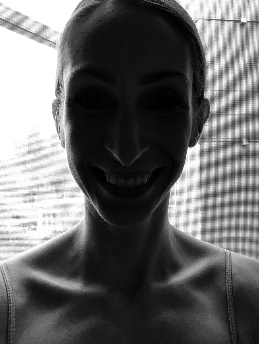 Silhouette of a person smiling in front of a window with grid patterns, creating a high contrast image.