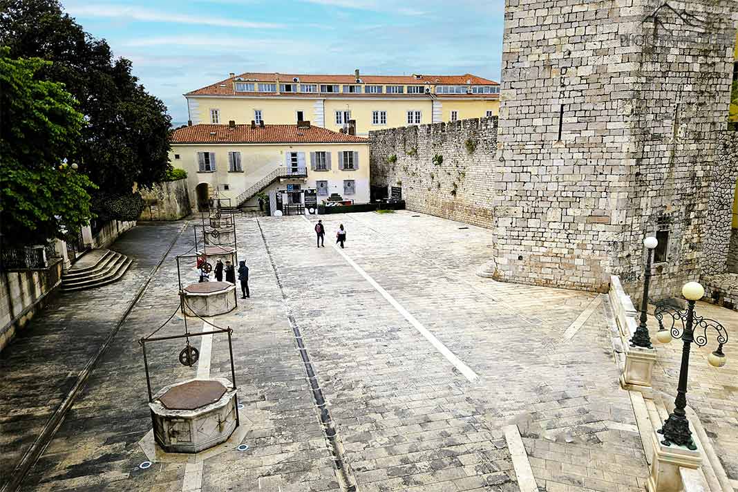 Einige Besucher laufen über den Fünf-Brunnen-Platz vorbei am Kapitänsturm