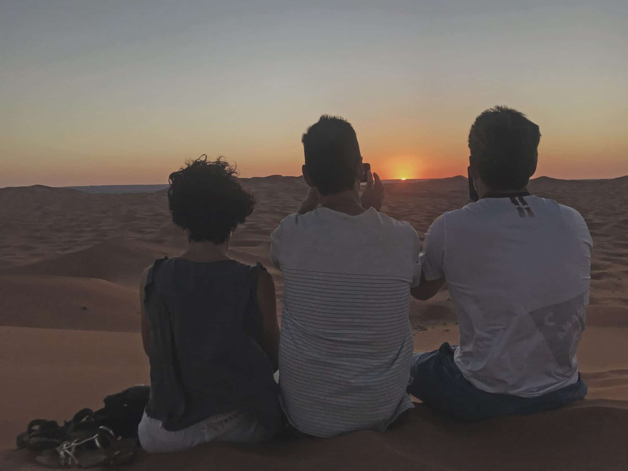Espectacular vista del atardecer en el desierto con tres personas disfrutando del paisaje.