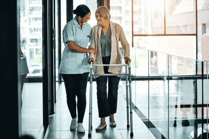 Specialized and Extended Care for Seniors | Professional Elderly Support Services.png Caregiver assisting a senior woman with a walker, symbolizing specialized and extended care services, including elderly care and daily living assistance.