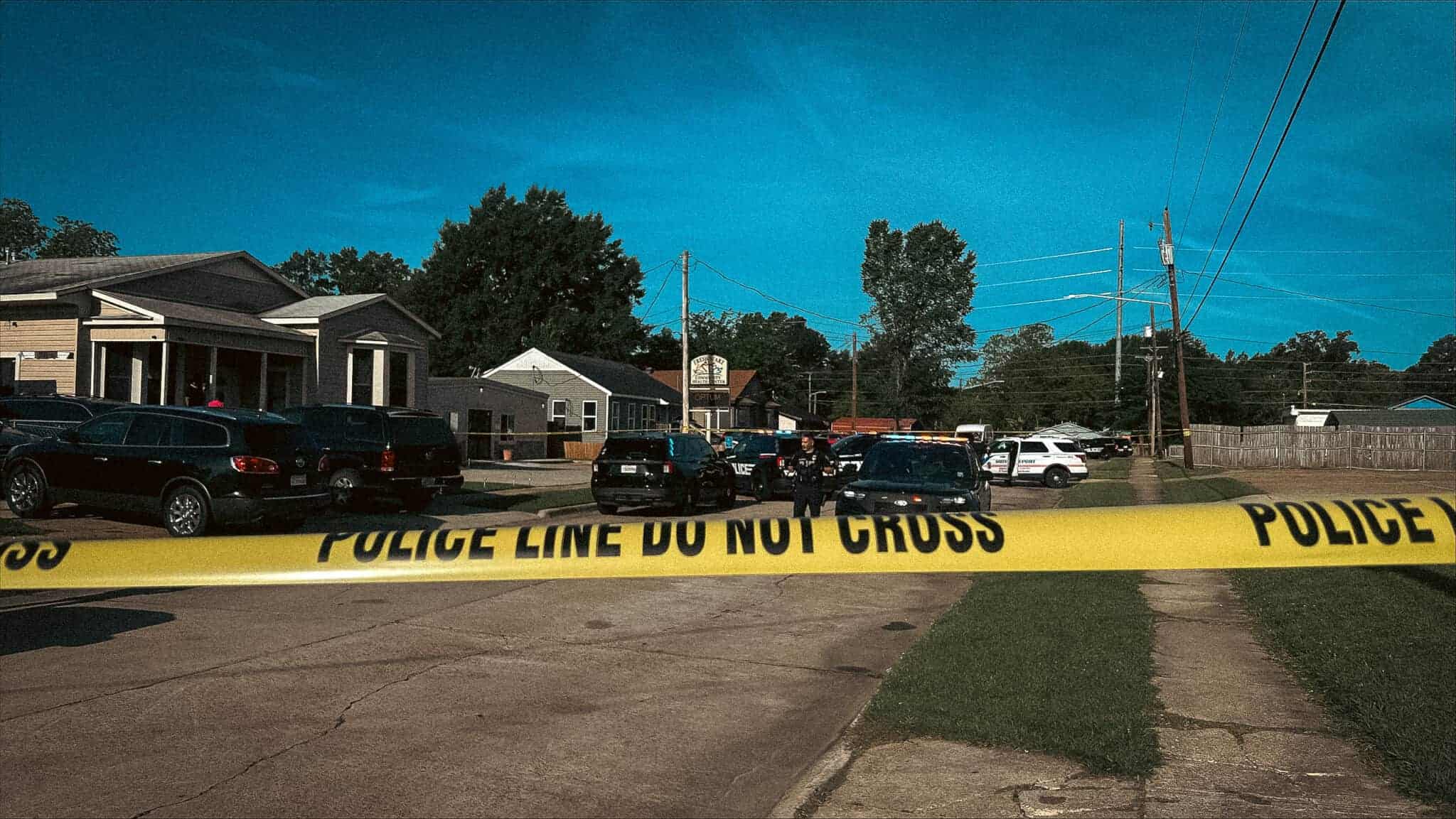 Yellow police tape across a residential street with patrol cars outside a house.