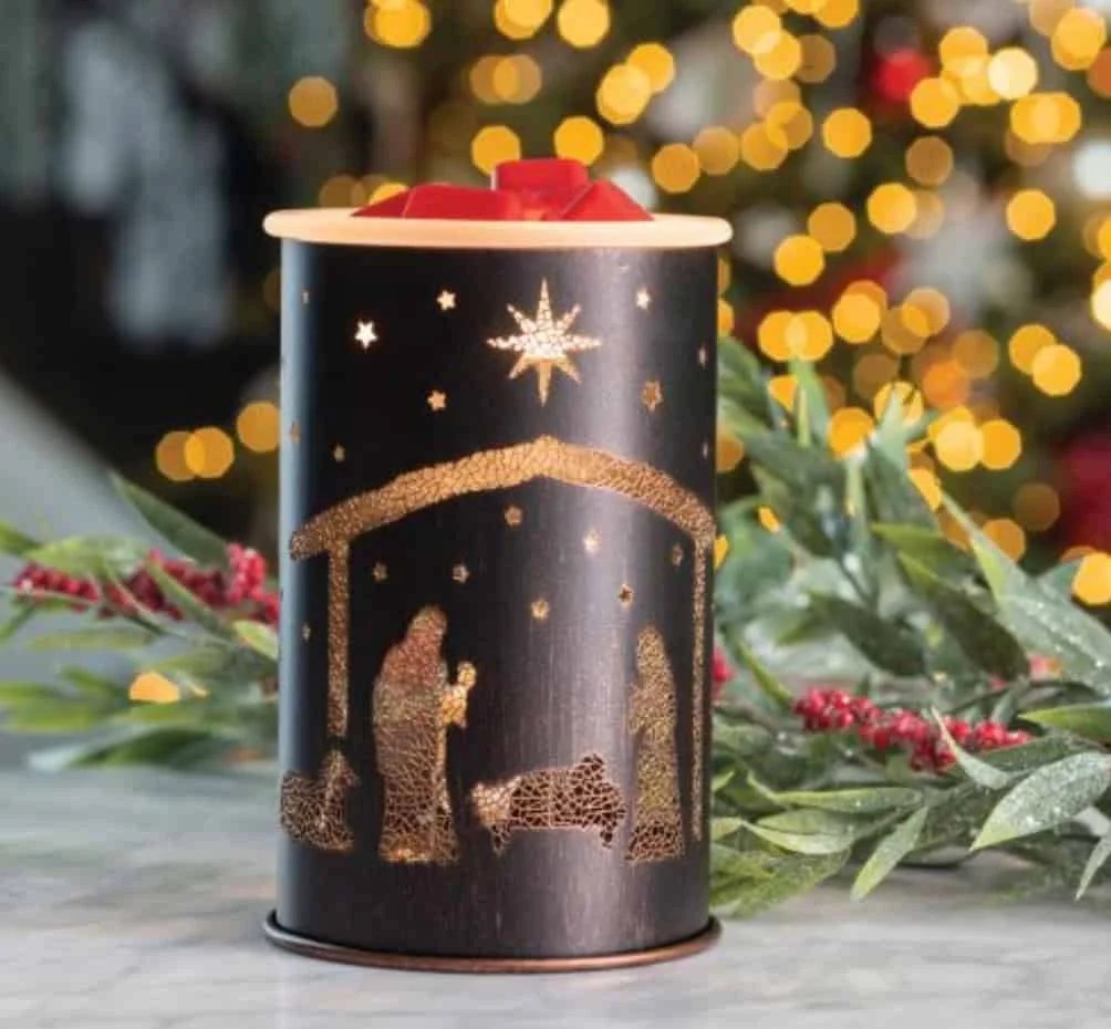 Christmas Gmones in Lights Classic T-Shirt 13 The Nativity Wax Warmer with a nativity scene cutout sits on a marble surface, accented by greenery and red berries, with blurred Christmas lights glowing in the background.