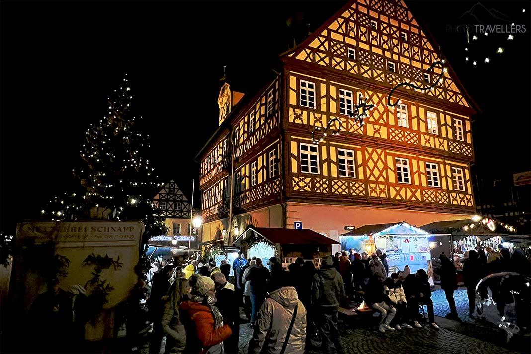 Vor dem beleuchteten Fachwerkrathaus in Bad Staffelstein stehen viele Menschen an den Weihnachtsständen