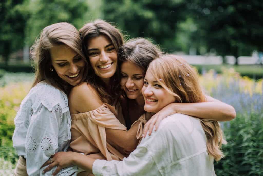 A group of four young women hugging each other tightly and smiling; they appear very close.