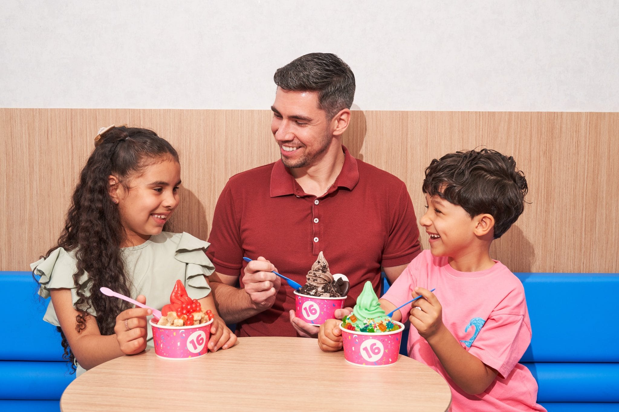 Father and two children enjoying colorful 16 Handles frozen yogurt cups together at a table inside a store