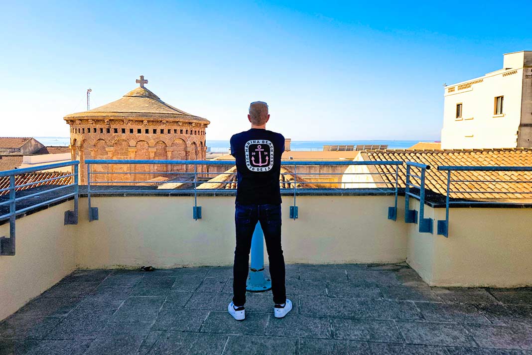 Ein blonder Mann mit Jeans und T-Shirt steht mit dem Rücken zur Kamera und blickt über die Dächer von Taranto