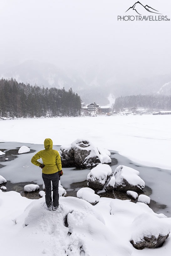 Reisebloggerin Biggi Bauer steht im Winter mit einer gelben Jacke am Eibsee-Ufer und blickt über den zugefrorenen See