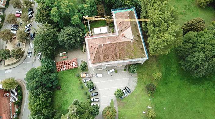 Luftaufnahme eines Gebäudes mit braunem Dach, mehreren geparkten Autos und Bäumen in einem kleinen Parkplatzbereich.