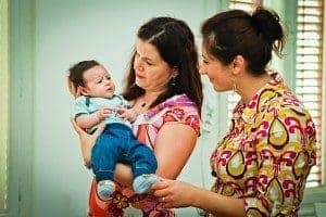 GOKID! - Îngrijire și educație pentru copii Fetiță ținând în brațe un bebeluș, înconjurată de o femeie și o femeie, într-un mediu cald și priete.
