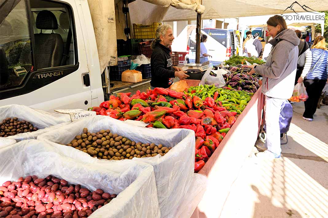 Ein Händler steht hinter seinem Gemüsestand und spricht mit einem Mann am Markt von Kassandria