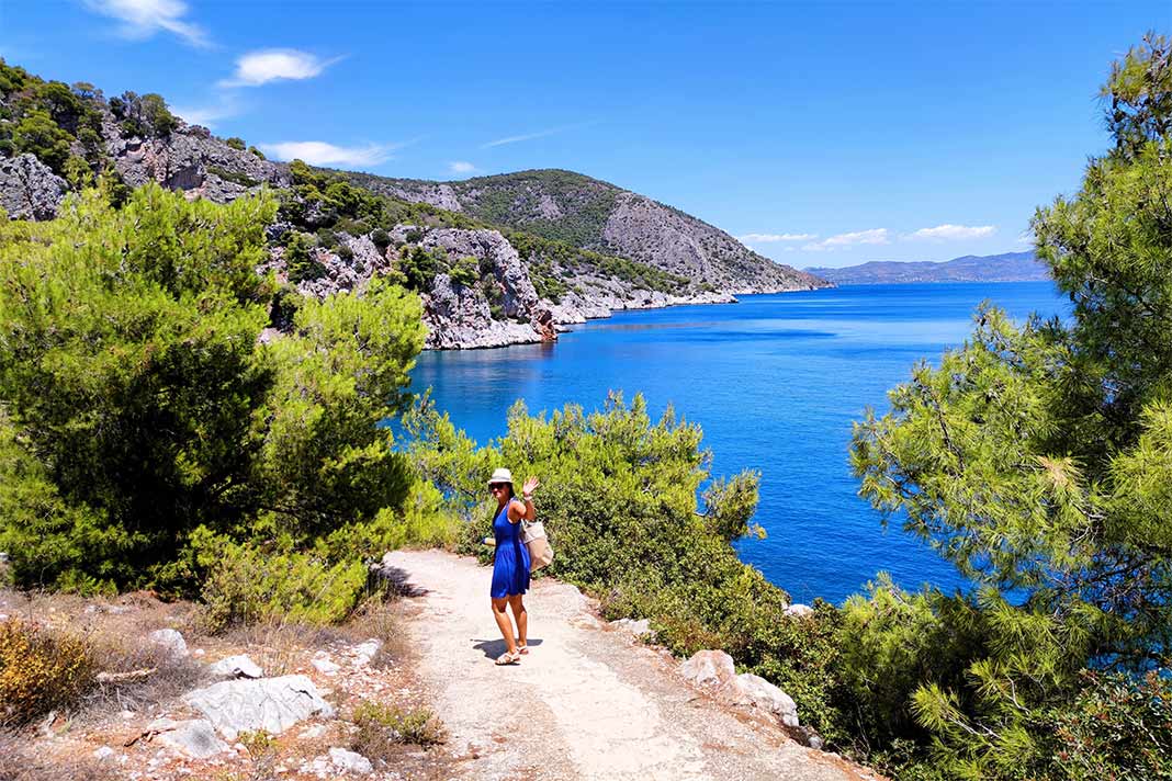 Ein Frau im blauen Kleid winkt auf dem Weg überhalb der felsigen Bucht von Limenaria
