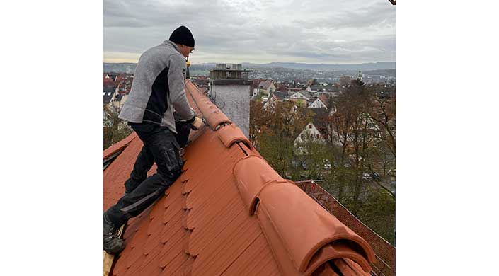 Rotes Ziegeldach mit Blick auf eine Stadt, bewölkter Himmel, im Hintergrund Häuser und Bäume.
