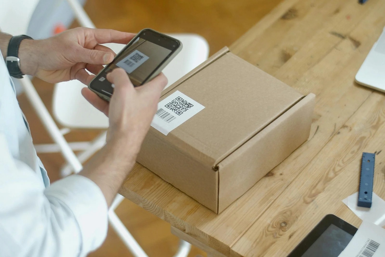 Smartphone scanning a QR code next to a delivery parcel, representing the link between mobile browsing and online shopping habits.