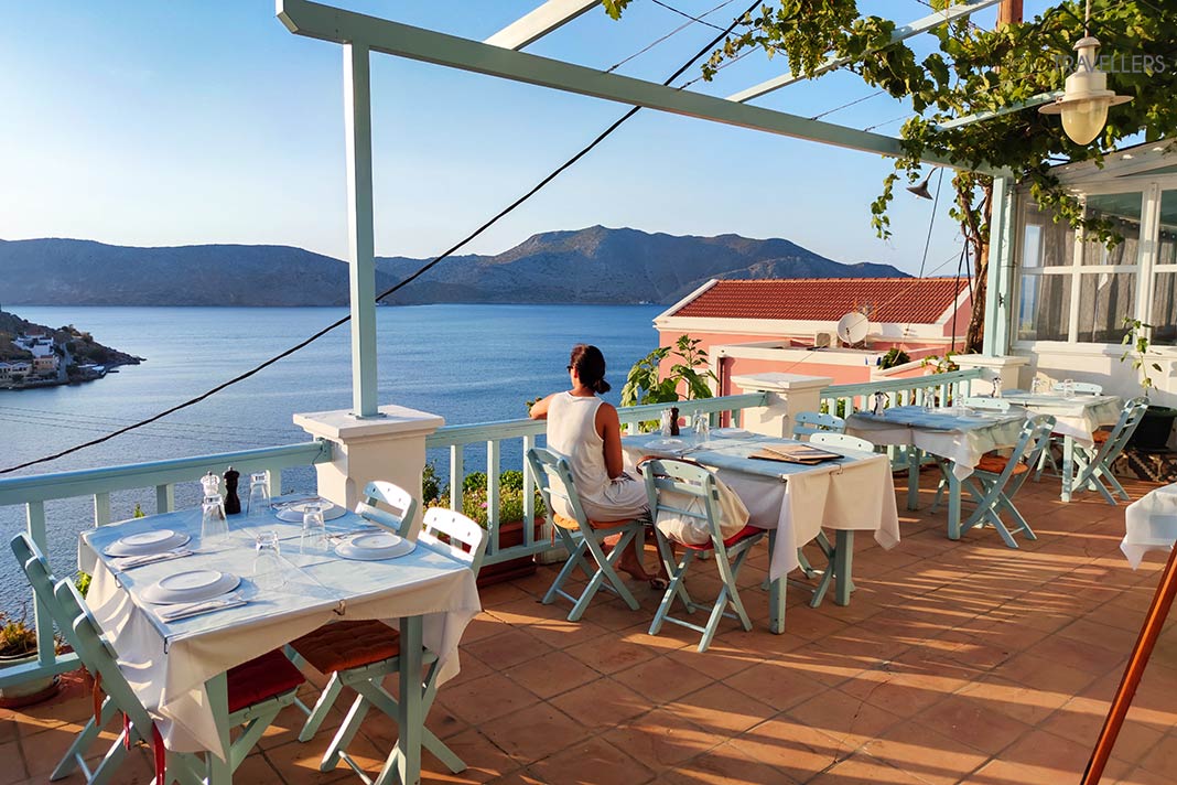 Eine Frau sitzt am Essenstisch auf einer Terrasse hoch über dem Meer