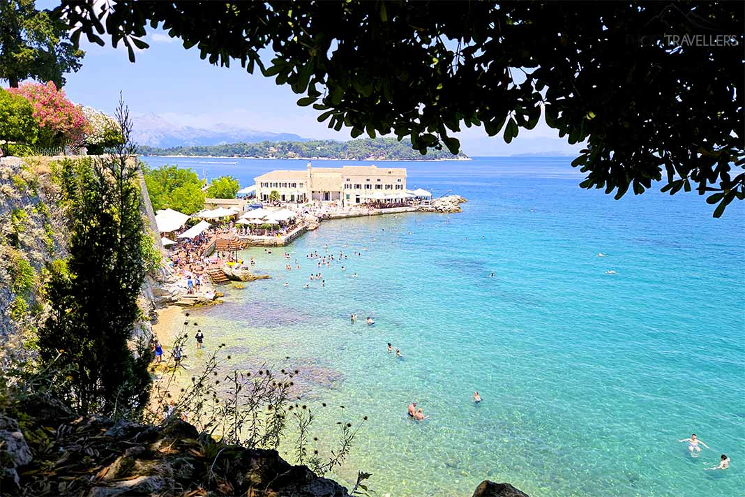 Zwischen Felsen, Bäumen und Meer tummeln sich viele Badegäste am Faliraki Beach in Kerkyra