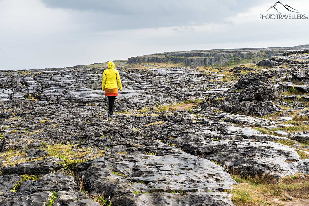 Reisebloggerin Biggi Bauer in gelber Regenjacke auf Felsen in der Burren-Landschaft, Irland