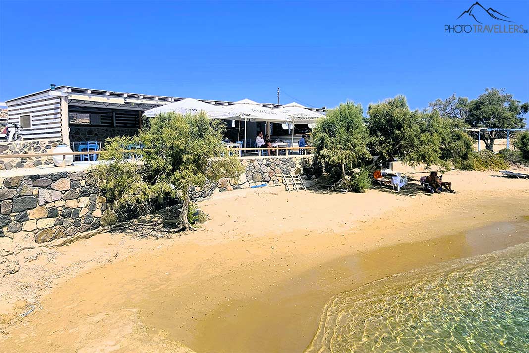 Unter den Schirmen sitzen Gäste einer Taverne direkt oberhalb des Sandstrands von Kalamitsi