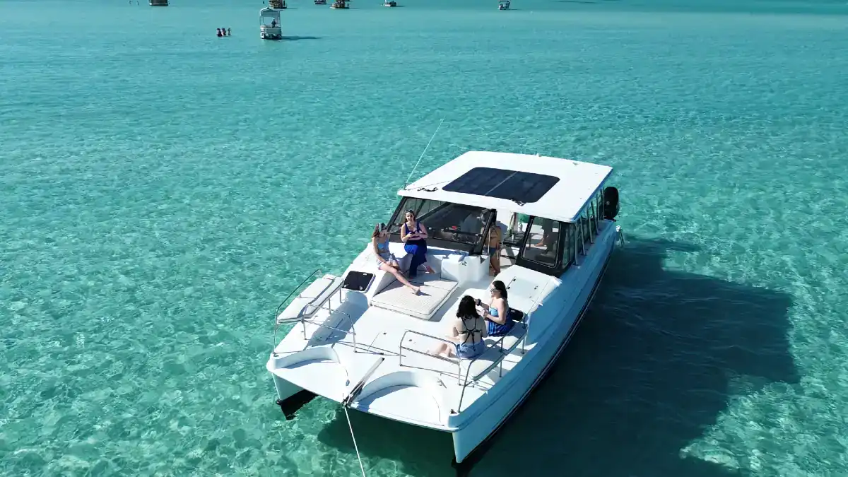 Luxury White Catamaran anchored at Crab Island with a group of girls lounging on the front deck.